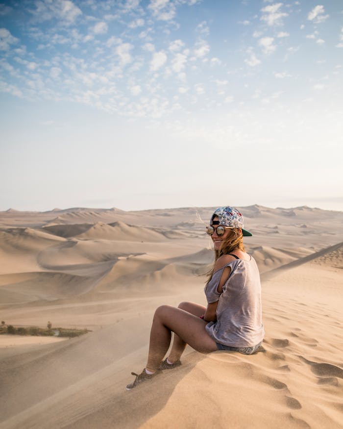 pexels-photo-7435824 A woman sits on a sand dune overlooking the vast Huacachina desert landscape.